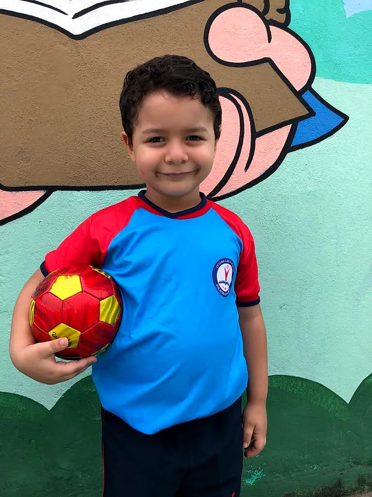 Aluno de uniforme segurando uma bola de futsal